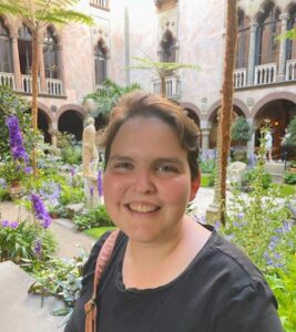 Woman smiling in a black t-shirt. Standing in from of a flower garden