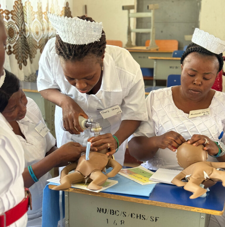 Three nurses around a table with plastic babies practicing resuscitating babies