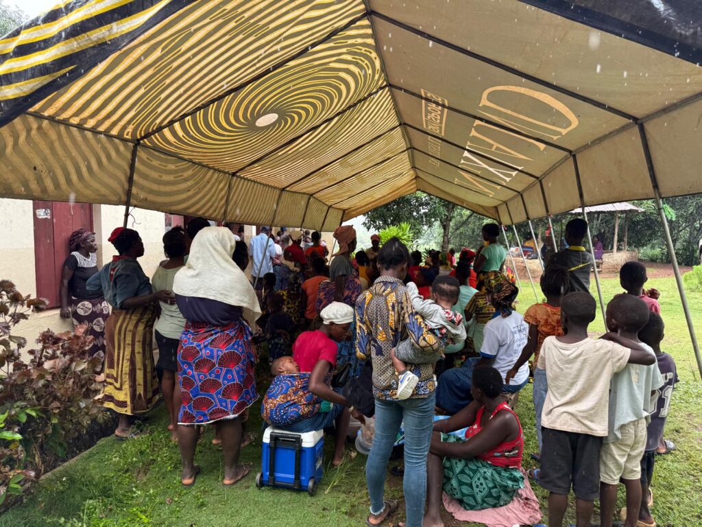 A crowd of people under a tent waiting for treatment in a village