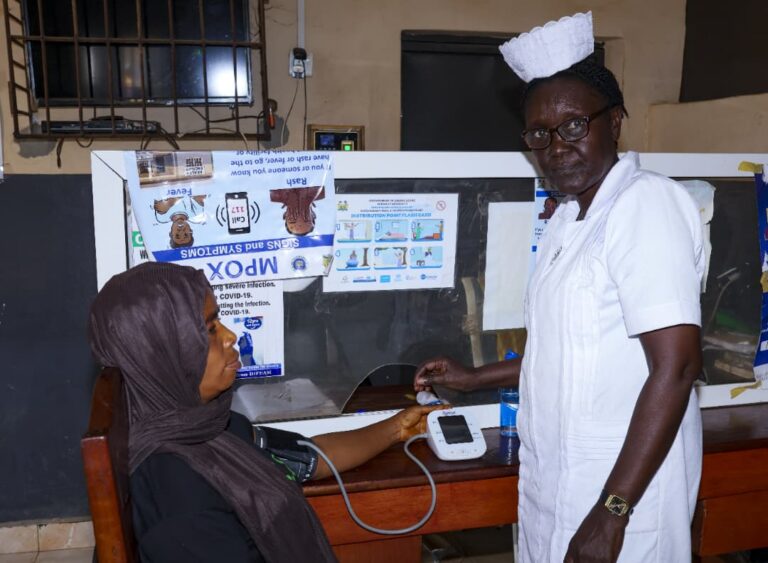 A nurse is taking the blood pressure of a woman sitting in a chair